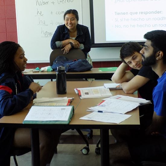 A Latina instructor with a stands over a small mixed gender, diverse group of UIC students