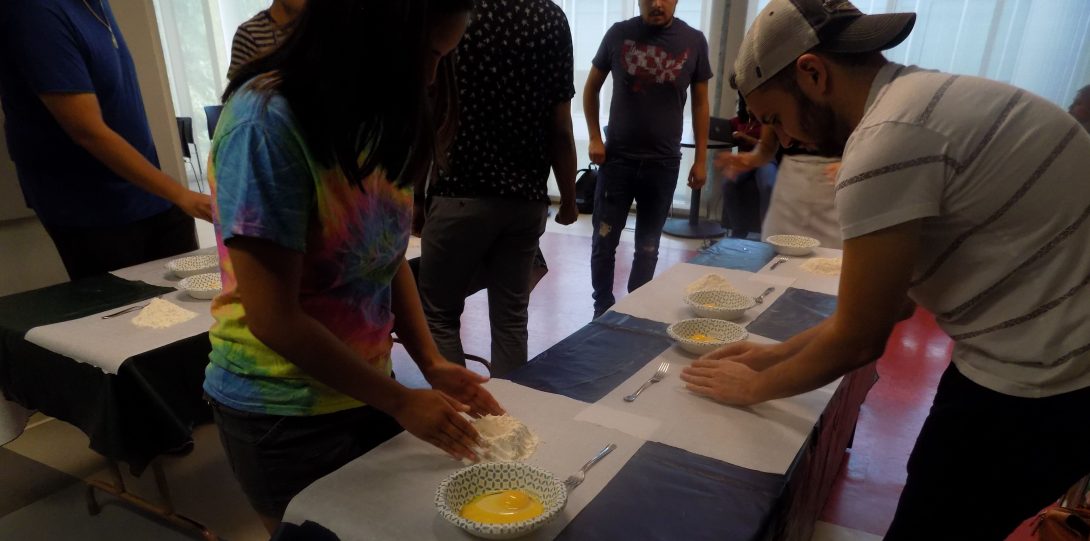 a mixed group of students works with flour and eggs on a table to make dough