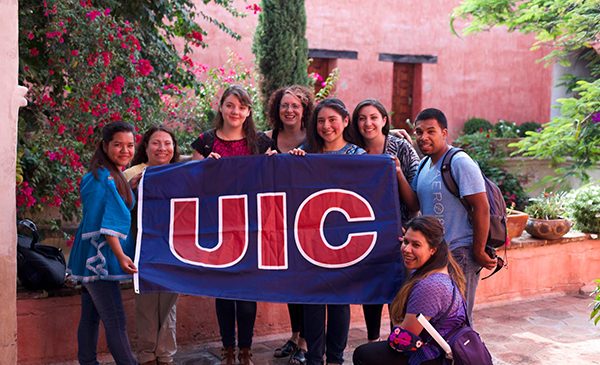 mixed group of students and faculty holding a blue and red UIC flag